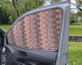May include: A car window with a patterned window shade. The shade is made of a fabric with a wavy pattern in shades of brown, orange, and gray.
