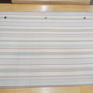 以下が含まれることがあります： トンボのロゴが付いた白とベージュのストライプの窓のシェード。シェードは薄いグレーの縁取りと3つの小さな黒いボタンが付いています。