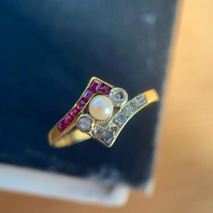 Puede incluir: Un anillo de oro con una sola perla y piedras de rubí engastadas en un diseño geométrico.