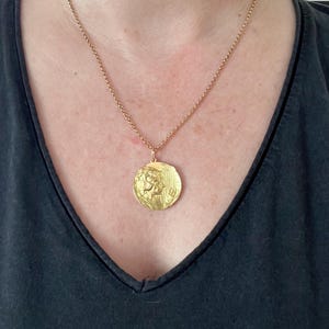 May include: A gold chain necklace with a large, round pendant featuring a detailed embossed design of a woman's face and a harp.