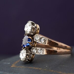 May include: A gold ring with a blue sapphire and two white diamonds. The ring is set on a blue velvet surface.