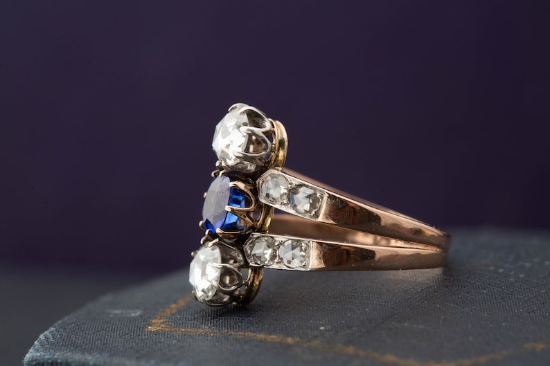 May include: A gold ring with a blue sapphire and two white diamonds. The ring is set on a blue velvet surface.
