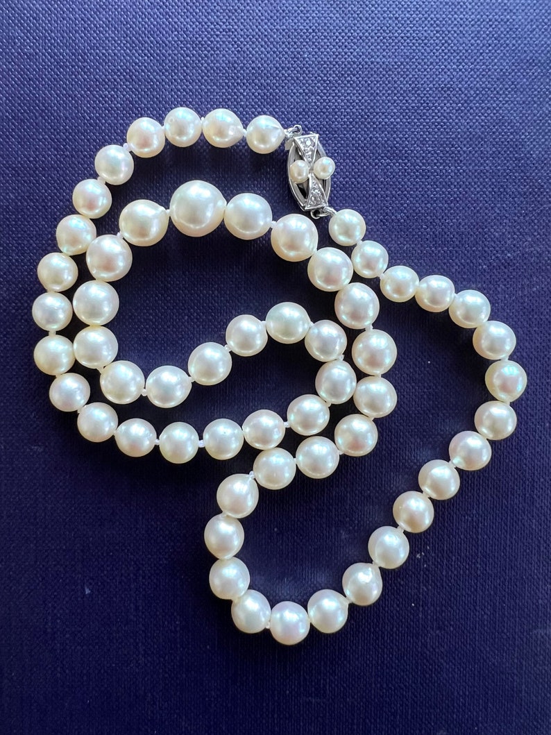 May include: A strand of white pearls with a silver clasp. The pearls are strung on a white thread and are arranged in a circular pattern. The clasp is a small, silver piece with a diamond-shaped design.