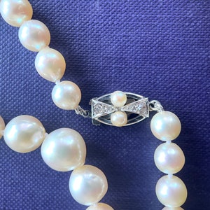 May include: A white pearl necklace with a silver clasp set with small diamonds. The pearls are round and smooth, and the necklace is strung on a delicate chain.