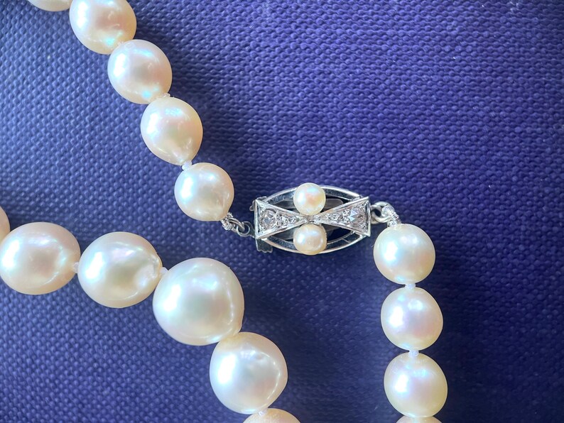 May include: A white pearl necklace with a silver clasp set with small diamonds. The pearls are round and smooth, and the necklace is strung on a delicate chain.