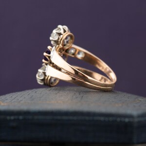 May include: A gold ring with a cluster of purple and white gemstones. The ring is set on a black velvet box.