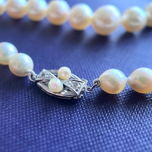 May include: A pearl necklace with a silver clasp featuring small diamonds. The pearls are white and have a slight iridescent sheen.