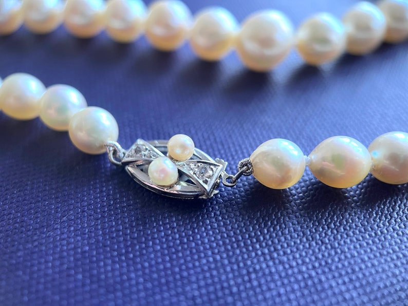 May include: A pearl necklace with a silver clasp featuring small diamonds. The pearls are white and have a slight iridescent sheen.
