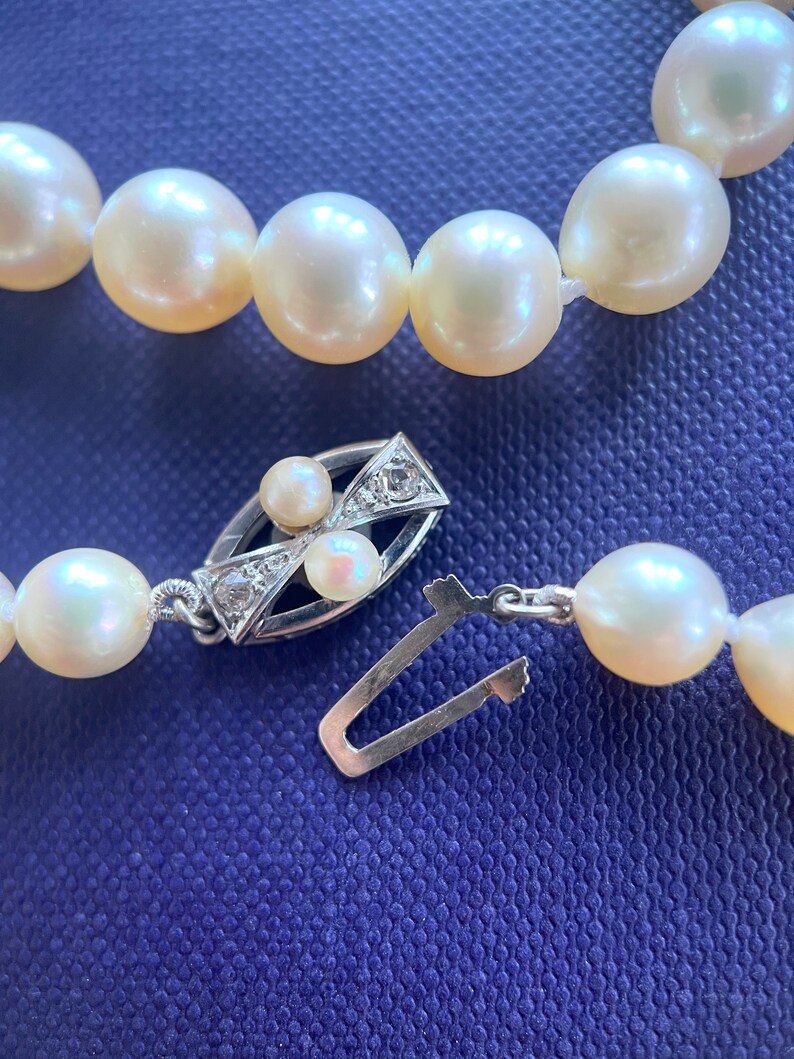 May include: A white pearl necklace with a silver clasp featuring small diamonds. The necklace is on a blue background.