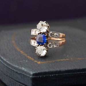 May include: A gold ring with a blue sapphire and two round diamonds. The ring is set on a blue velvet box.