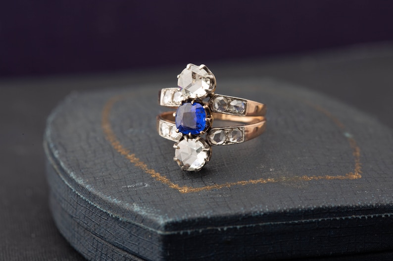May include: A gold ring with a blue sapphire and two round diamonds. The ring is set on a blue velvet box.