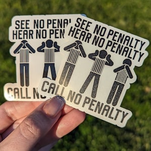 May include: Two silver stickers with black text and illustrations of referees with their hands over their eyes and ears. The text on the stickers reads "See no penalty, hear no penalty, call no penalty".