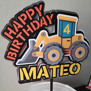 May include: A yellow and black construction vehicle cake topper with the words "Happy Birthday Mateo" and the number "4" on the side.
