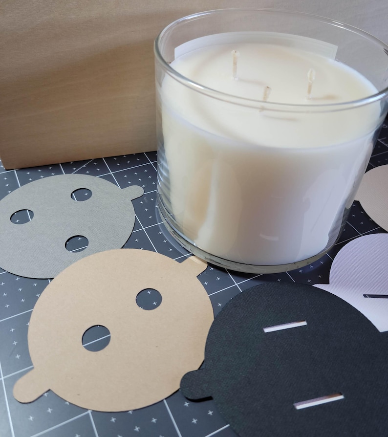 Overview of candle dust covers in a variety of color options, including black, white, cream, gray, and kraft brown. A silver tin candle is featured with a black dust cover in standard wick as an example.