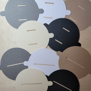 Overhead view of candle dust covers in black, gray, white, and cream on a wood background. Standard and wood wick options.