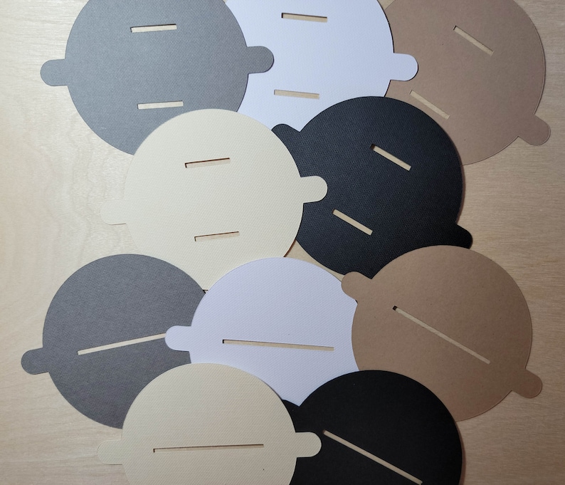Overhead view of candle dust covers in black, gray, white, and cream on a wood background. Standard and wood wick options.