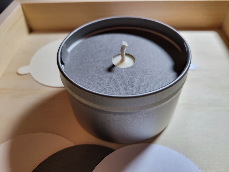 Overview of candle dust covers in a variety of color options, including black, white, cream, gray, and kraft brown. Focus is on a silver tin candle with a gray dust cover and a standard wick.