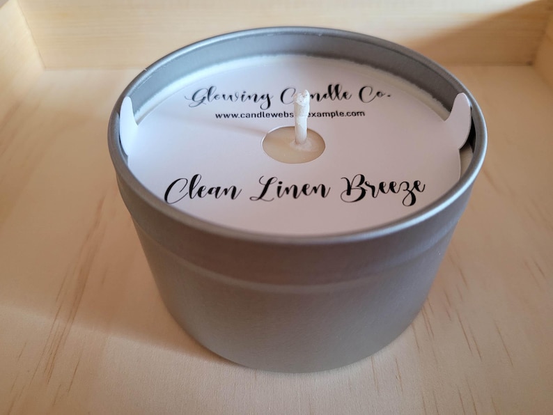 Photo featuring a sample of custom candle dust covers with mockup candle company name, candle ounces and type of wax, scent name Clean Linen Breeze and the standard remove lid before lighting text at the bottom. White cardstock black ink standard wick.