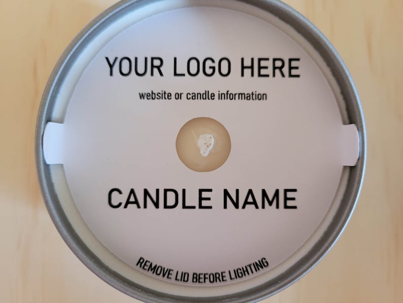Overhead view of sample for custom candle dust covers - white cardstock with black printing on a tin candle with a standard wick. Candle is sitting on a wood background.