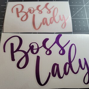 Photo featuring two examples of the Boss Lady vinyl decal - rose gold in 4-inches and purple sparkle in 5-inches - on a gray measuring mat for size.
