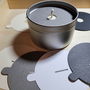 Overview of candle dust covers in a variety of color options, including black, white, cream, gray, and kraft brown. A silver tin candle with a gray dust cover in standard wick is featured.