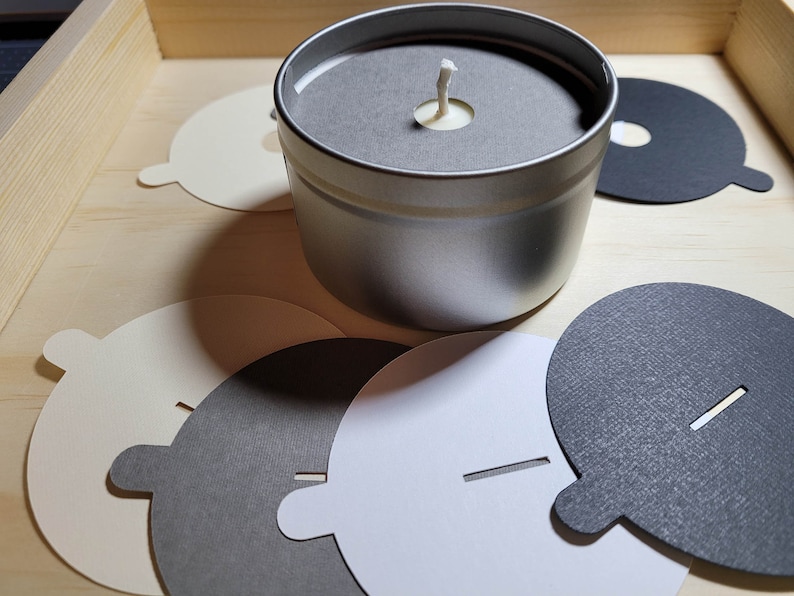 Overview of candle dust covers in a variety of color options, including black, white, cream, gray, and kraft brown. A silver tin candle with a gray dust cover in standard wick is featured.