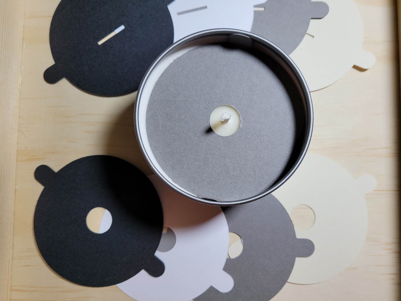 Overhead view of candle dust covers in black, gray, white, and cream on a wood background. Standard and wood wick options.