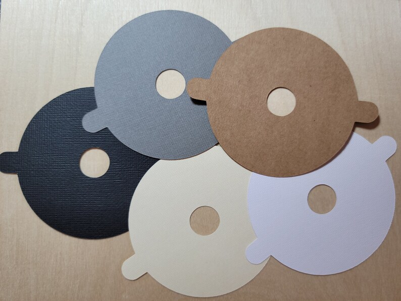 Overhead view of candle dust covers in black, gray, white, and cream on a wood background. Standard wick options.