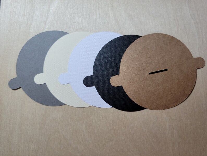 Overhead view of candle dust covers in black, gray, white, and cream on a wood background. Standard and wood wick options.