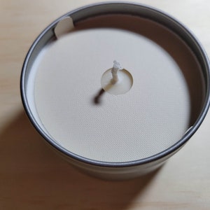 Overhead view of a silver tin candle with a cream colored dust cover and a standard wick.