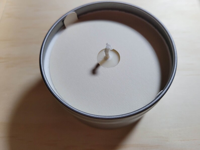 Overhead view of a silver tin candle with a cream colored dust cover and a standard wick.