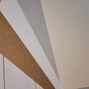 Photo showing the new and old versions of the kraft cover stock materials used for making custom candle dust covers. The newer version is a couple of shades darker and is actually more of a "true" kraft color.