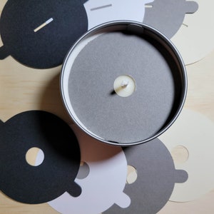 Overview of candle dust covers in a variety of color options, including black, white, cream, gray, and kraft brown. A silver tin candle with a gray dust cover in standard wick is featured.