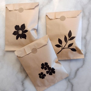 May include: Three brown paper bags with black floral designs. The bags have a circle sticker on the top.