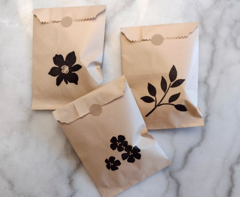 May include: Three brown paper bags with black floral designs. The bags have a circle sticker on the top.