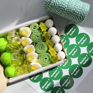 May include: A green and white gift box filled with green and white gummy sweets, including gummy rings, gummy eggs, and gummy bears. The box is surrounded by green and white round stickers that say "Number 1 Golfer!"