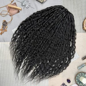 May include: A set of long, black, wavy synthetic hair extensions with a textured, crimped appearance. The hair is arranged in a dense, voluminous cluster, showcasing a deep black color throughout the strands, which feature a consistent, wavy pattern from the top down to the tapered ends.