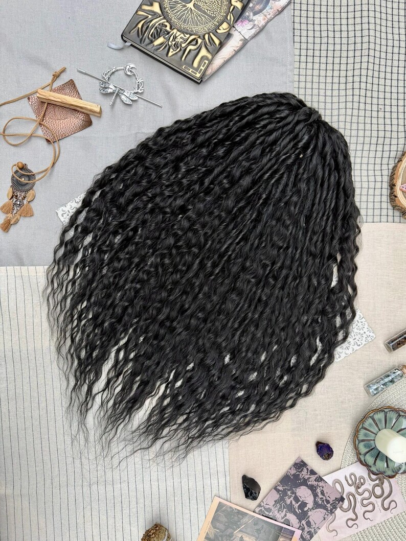 May include: A set of long, black, wavy synthetic hair extensions with a textured, crimped appearance. The hair is arranged in a dense, voluminous cluster, showcasing a deep black color throughout the strands, which feature a consistent, wavy pattern from the top down to the tapered ends.