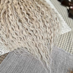 Pu&ograve; includere: Una lunga extension per capelli ondulati in una tonalit&agrave; biondo platino chiaro. I capelli presentano una consistenza densa e crespa con ciocche sottili che si assottigliano verso il basso, creando un aspetto voluminoso e stratificato con un movimento naturale.