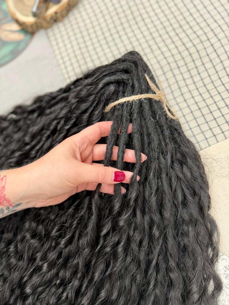 May include: A bundle of black synthetic hair extensions featuring a wavy, textured finish. The individual strands are gathered together and secured at the top with a piece of natural-colored twine, creating a uniform and organized hair piece.