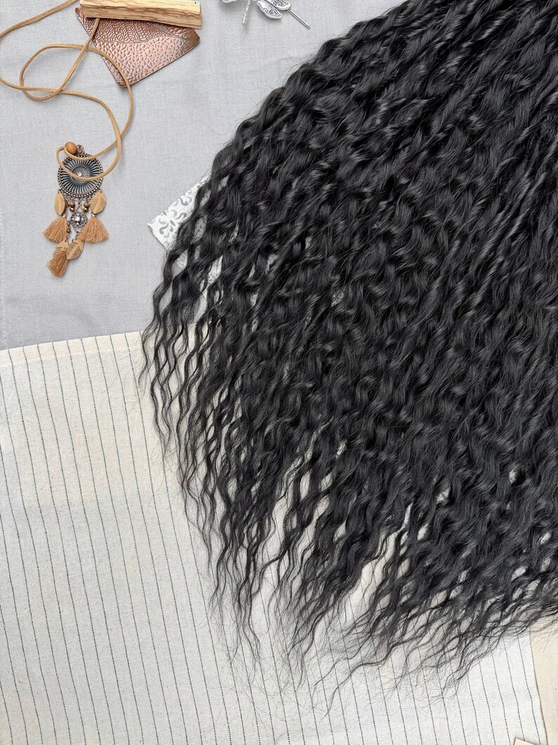 May include: A bundle of long, black, wavy hair extensions with a crimped texture. The hair is arranged in a dense, flowing mass, showcasing a consistent dark color and a defined, wavy pattern throughout the length of the strands.