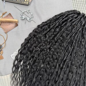 May include: A bundle of long, black synthetic hair extensions with a wavy, textured finish. The hair strands are tightly coiled and layered, creating a voluminous appearance. The dark black color is consistent throughout the entire length of the hair.