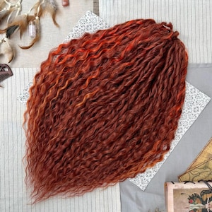 May include: A bundle of synthetic hair extensions featuring a vibrant mix of deep auburn and bright copper tones. The hair is styled in tight, wavy, crimped strands that create a voluminous, textured appearance with a consistent wavy pattern.