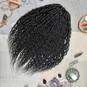 May include: A set of long, black, wavy synthetic hair extensions with a textured, crimped appearance. The hair is arranged in a dense, flowing cluster, showcasing individual strands with a consistent dark color and a natural-looking sheen.