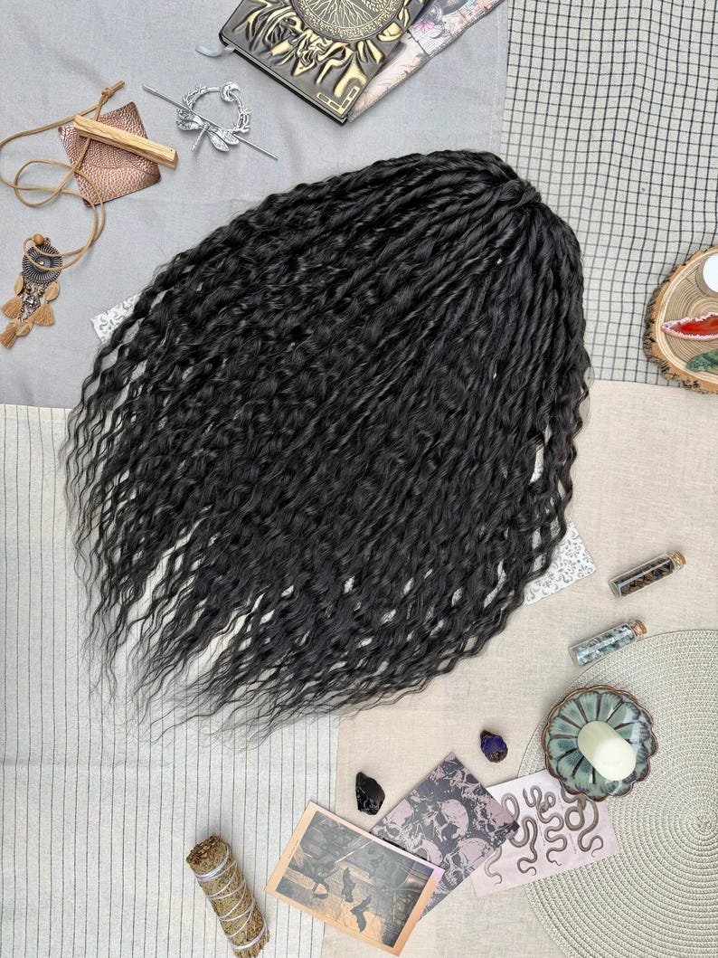 May include: A set of long, black, wavy synthetic hair extensions with a textured, crimped appearance. The hair is arranged in a dense, flowing cluster, showcasing individual strands with a consistent dark color and a natural-looking sheen.