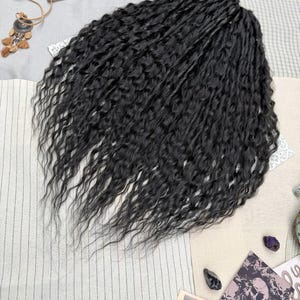 May include: A set of black synthetic hair extensions featuring a wavy, textured pattern. The hair is arranged in a dense, voluminous cluster with individual strands showing a consistent dark black color and a crimped, wavy appearance throughout.