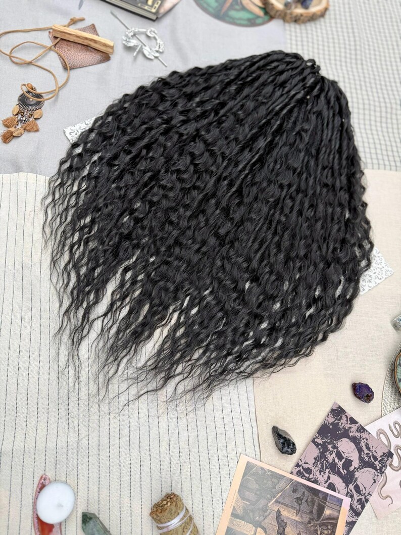 May include: A set of black synthetic hair extensions featuring a wavy, textured pattern. The hair is arranged in a dense, voluminous cluster with individual strands showing a consistent dark black color and a crimped, wavy appearance throughout.