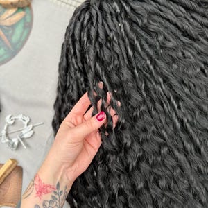 May include: A set of long, black synthetic hair extensions styled in tight, uniform twists. The hair features a consistent, wavy texture throughout each individual strand, creating a voluminous and layered appearance with a deep, dark black color.