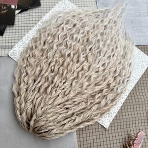 Pu&ograve; includere: Un set di extension per capelli sintetici biondo chiaro e ondulati, disposti a ventaglio. Le singole ciocche sono strettamente attorcigliate in ricci uniformi e crespi che si assottigliano verso l'alto, creando un aspetto voluminoso.
