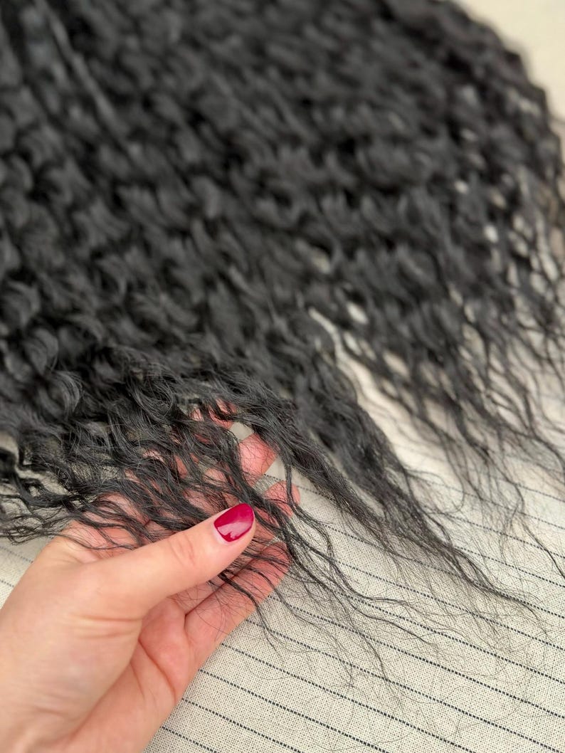 May include: A bundle of long, black hair extensions with a distinct wavy texture. The strands are fine and dark, showcasing a natural-looking curl pattern that flows downward. The hair appears soft and lightweight, with individual strands visible.